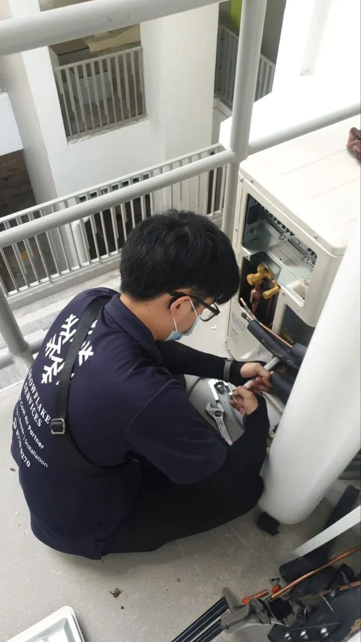 A Snowflake technician repairing a condenser unit on an HDB ledge.