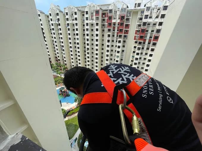 Technician in a safety harness working at height on an HDB block