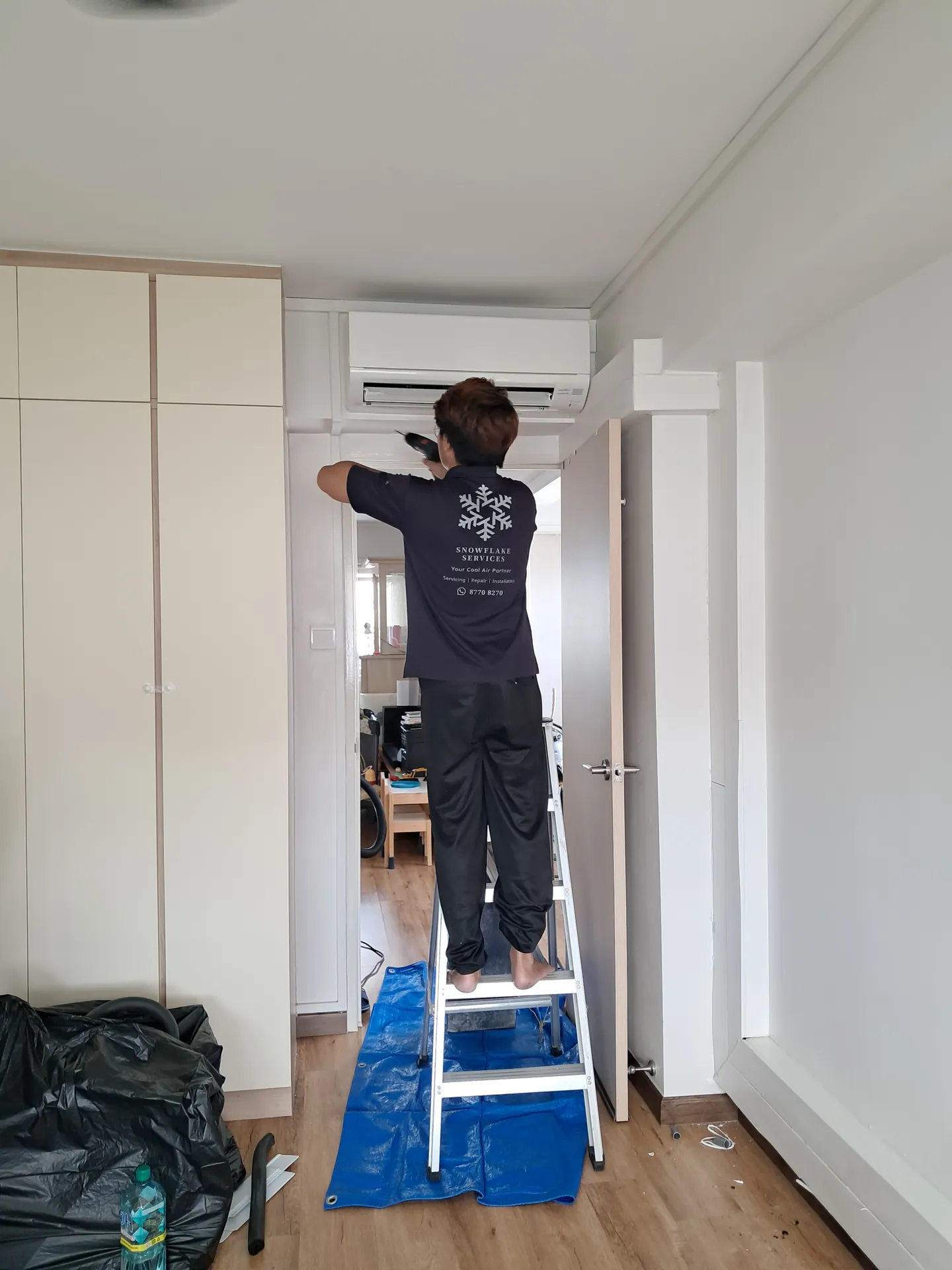 Technician on a step ladder servicing a wall-mounted unit in a bedroom