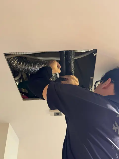 Technician working in a ceiling access hatch at ducts and pipes
