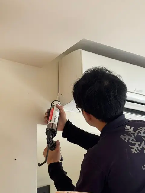 Technician using a sealant gun near a Mitsubishi Electric wall unit