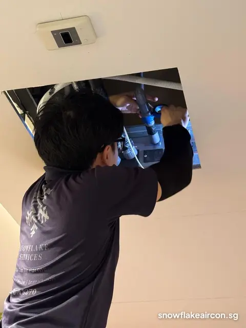 Technician reaching into a ceiling hatch at a ducted unit