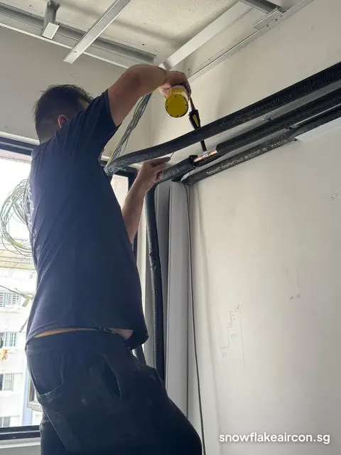 Technician at a window ledge with insulated pipe and a yellow tool