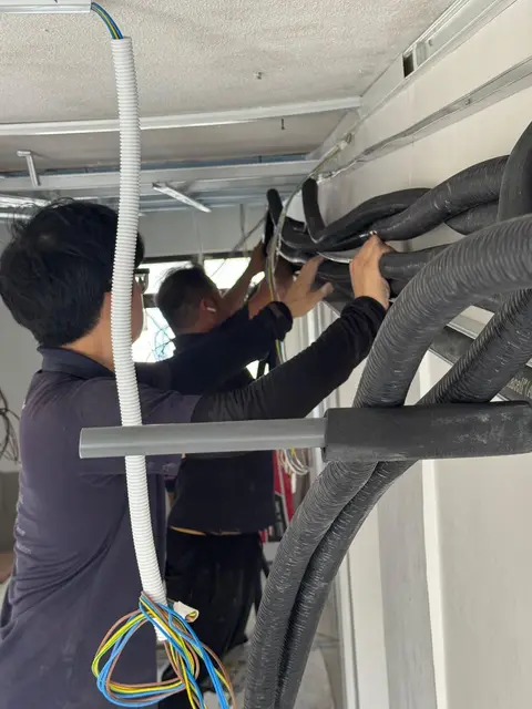 Two technicians routing bundled insulated pipes at a ceiling