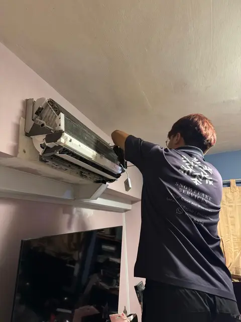 Technician in Snowflake shirt working on opened wall unit above a TV