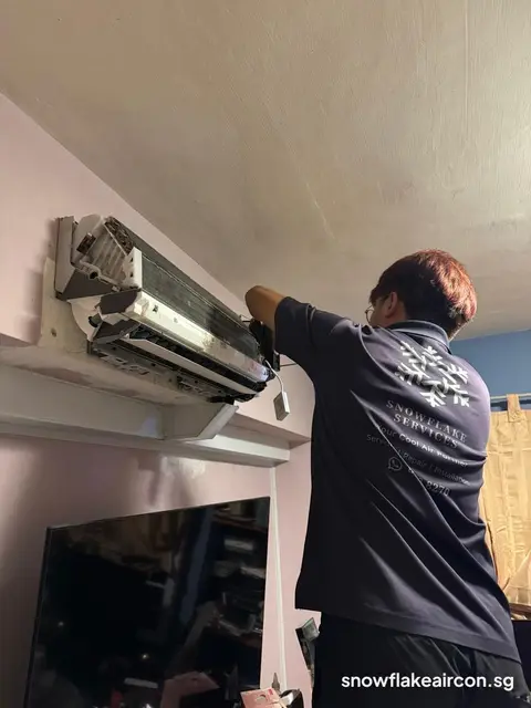 Technician in Snowflake shirt working on opened wall unit above a TV